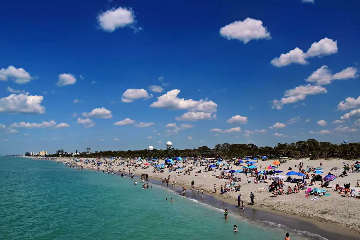 Aerial view of a wide white sand beach on the Gulf coast of Florida with turquoise shallow water and a line of umbrellas