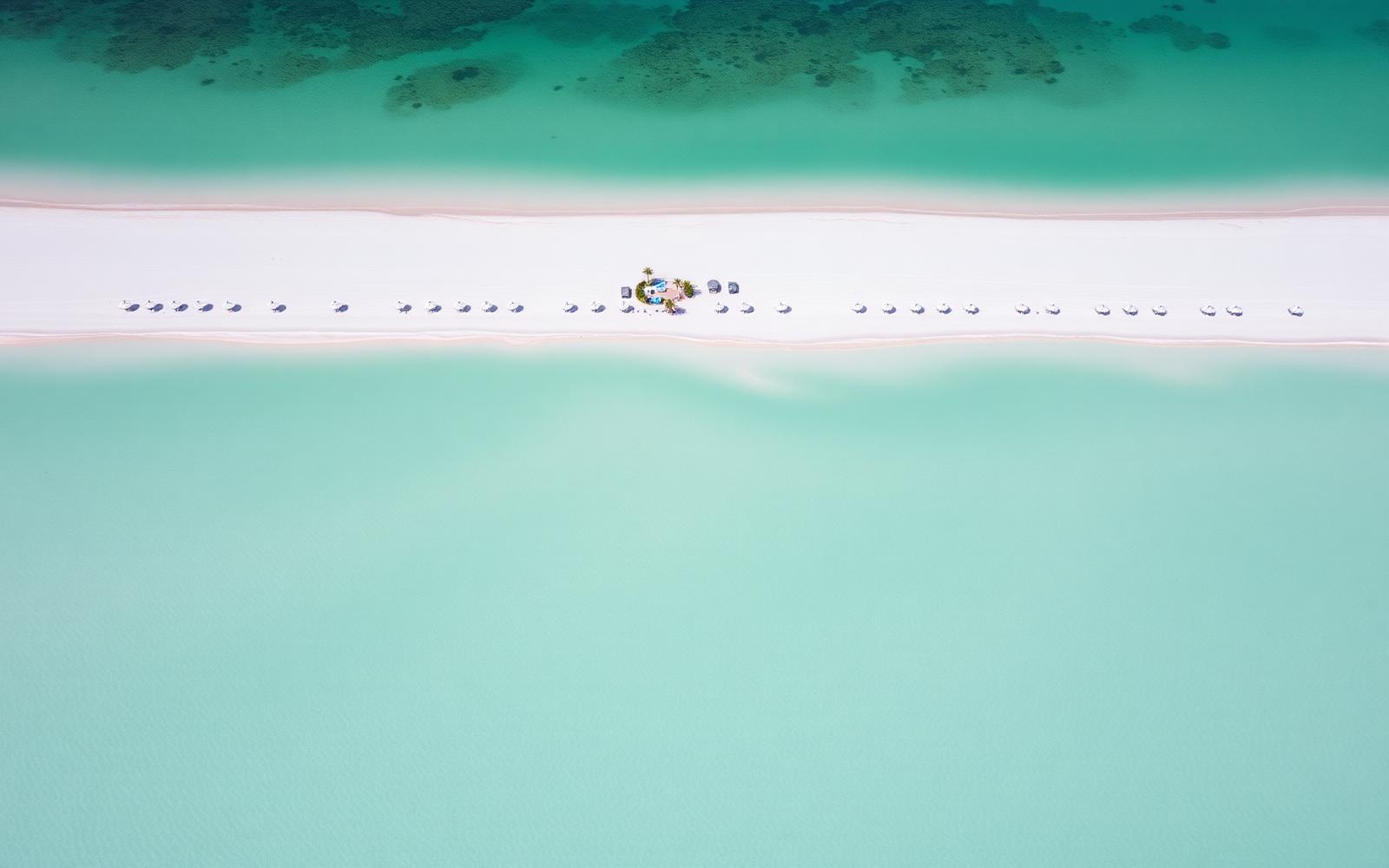 Aerial view of a wide white sand beach on the Gulf coast of Florida with turquoise shallow water and a line of umbrellas