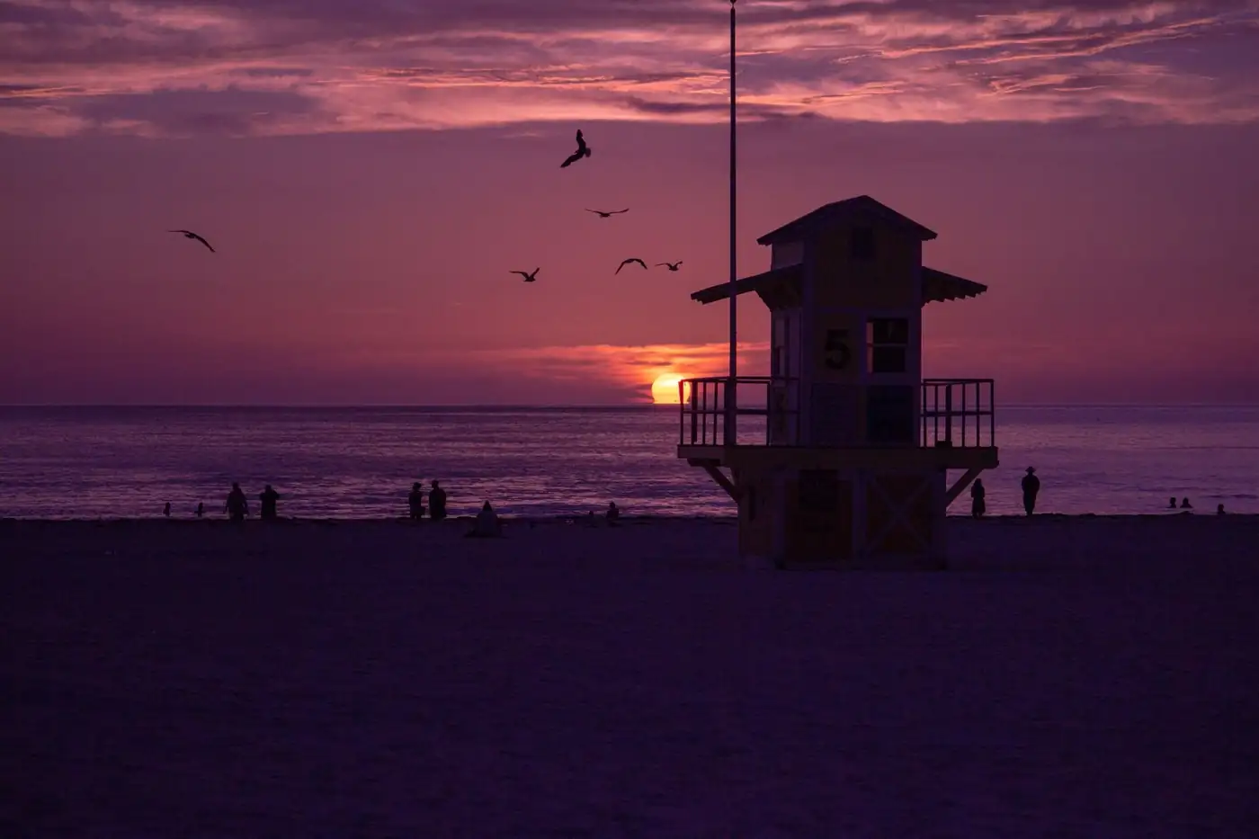 Orange and violet sunset over the Gulf of Mexico with the silhouette of Naples Pier and wet reflective sand